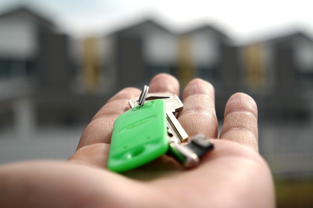 Keys in hand with residential property blurred in the background, representing buying and holding an investment property